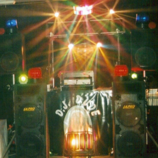 Small stage with speakers, DJ booth, and colorful lights shining above a banner backdrop.