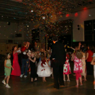 Children in formal clothes dance under falling confetti at an indoor party