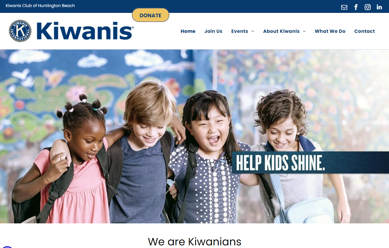 Four diverse children, smiling and embracing, in front of a school background. 