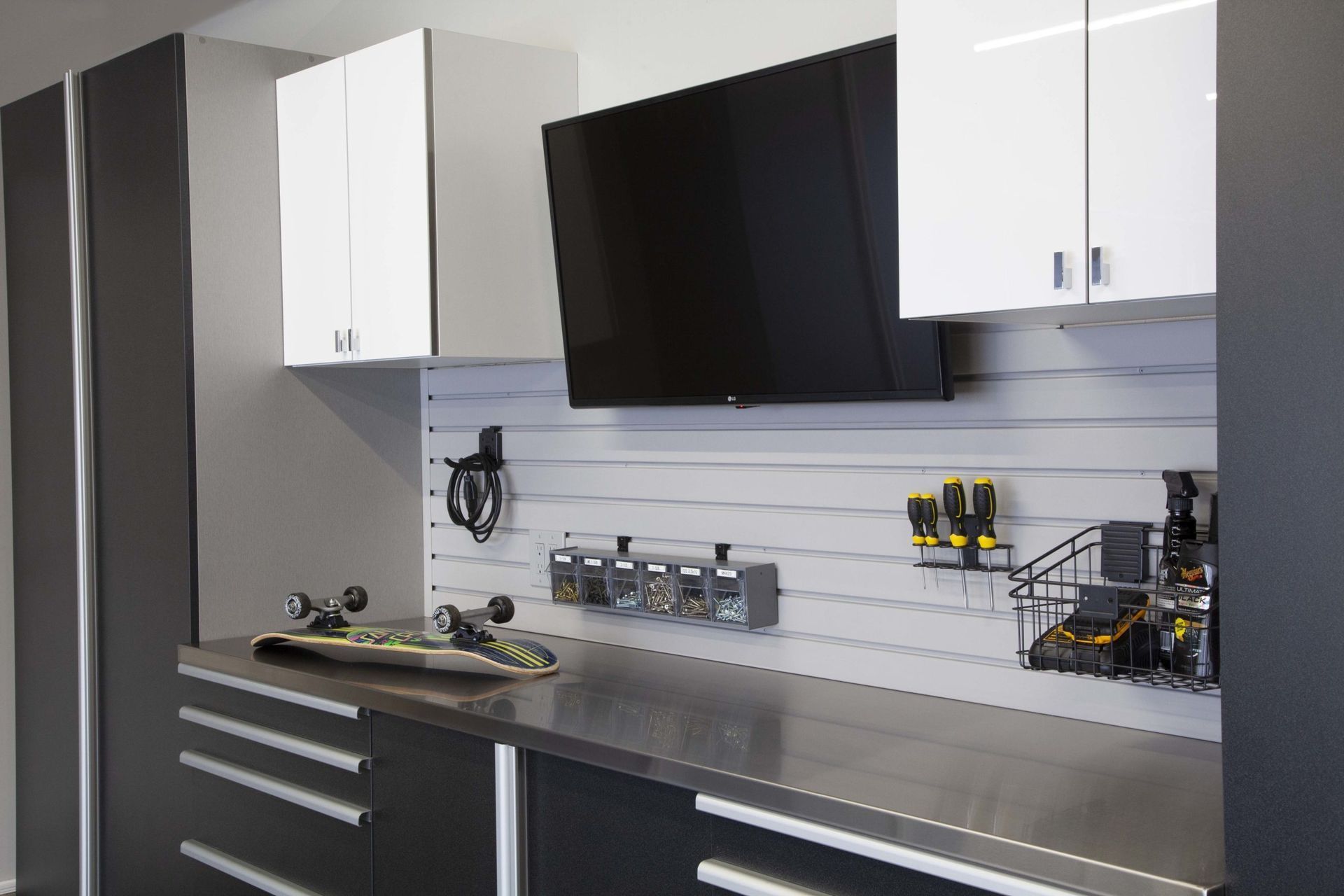 Garage workspace with cabinets, a stainless steel countertop, tools, and a mounted TV.