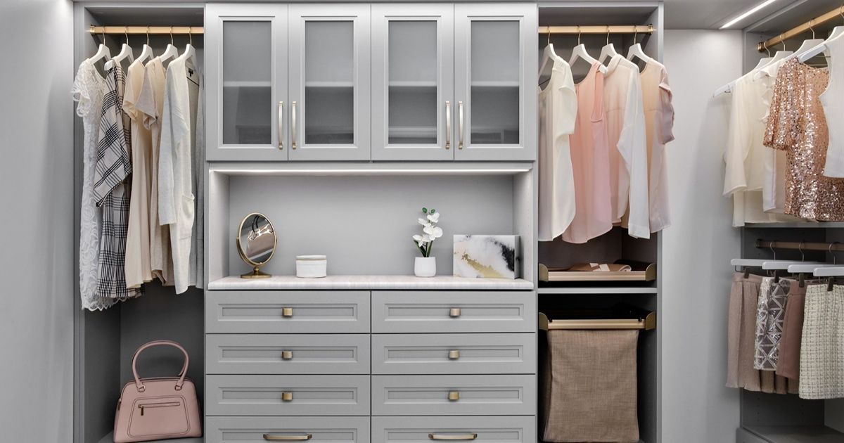 Gray walk-in closet with hanging clothes, drawers, cabinets, and a handbag.