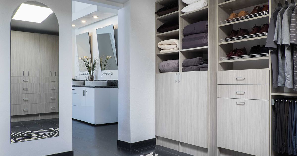 Walk-in closet with shelves, drawers, and a clothing rod, adjacent to a bathroom with mirrors and a sink.