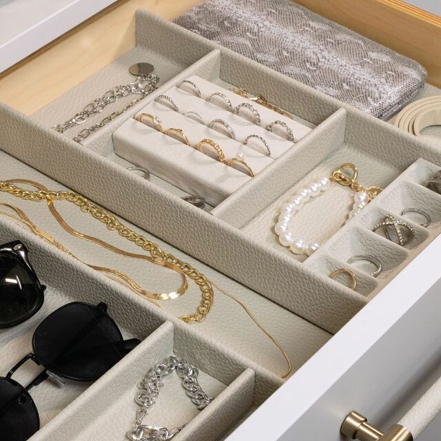 Drawer of jewelry in a closet, with clothes hanging nearby.
