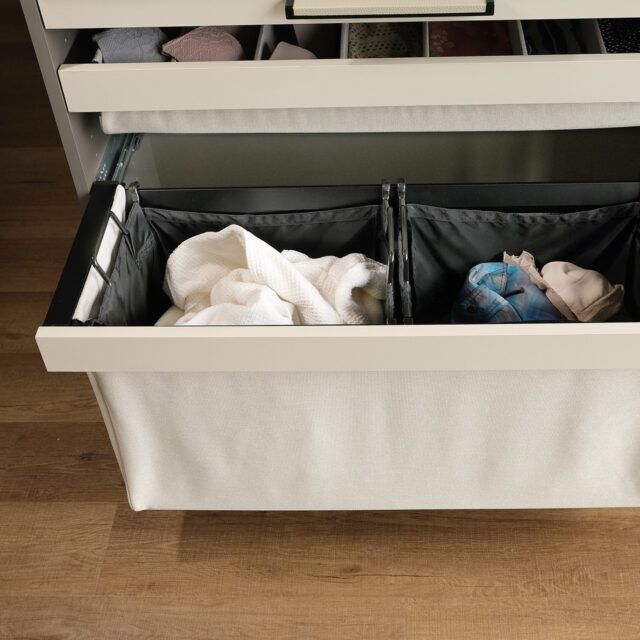 Gray fabric laundry hamper with two compartments, mounted in a closet. The hamper is pulled out on a track.