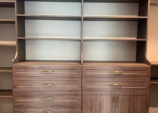 Closet organizer with shelves and drawers, brown wood finish, gold handles.
