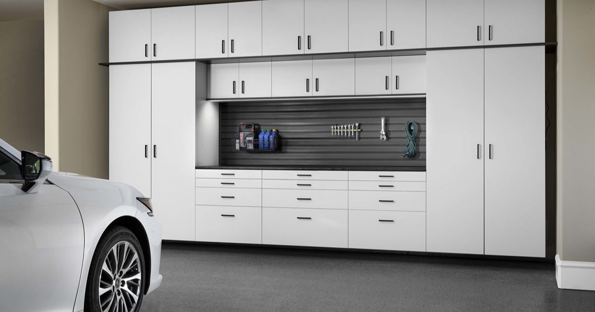 White garage storage cabinets with a workspace and a white car in the garage.