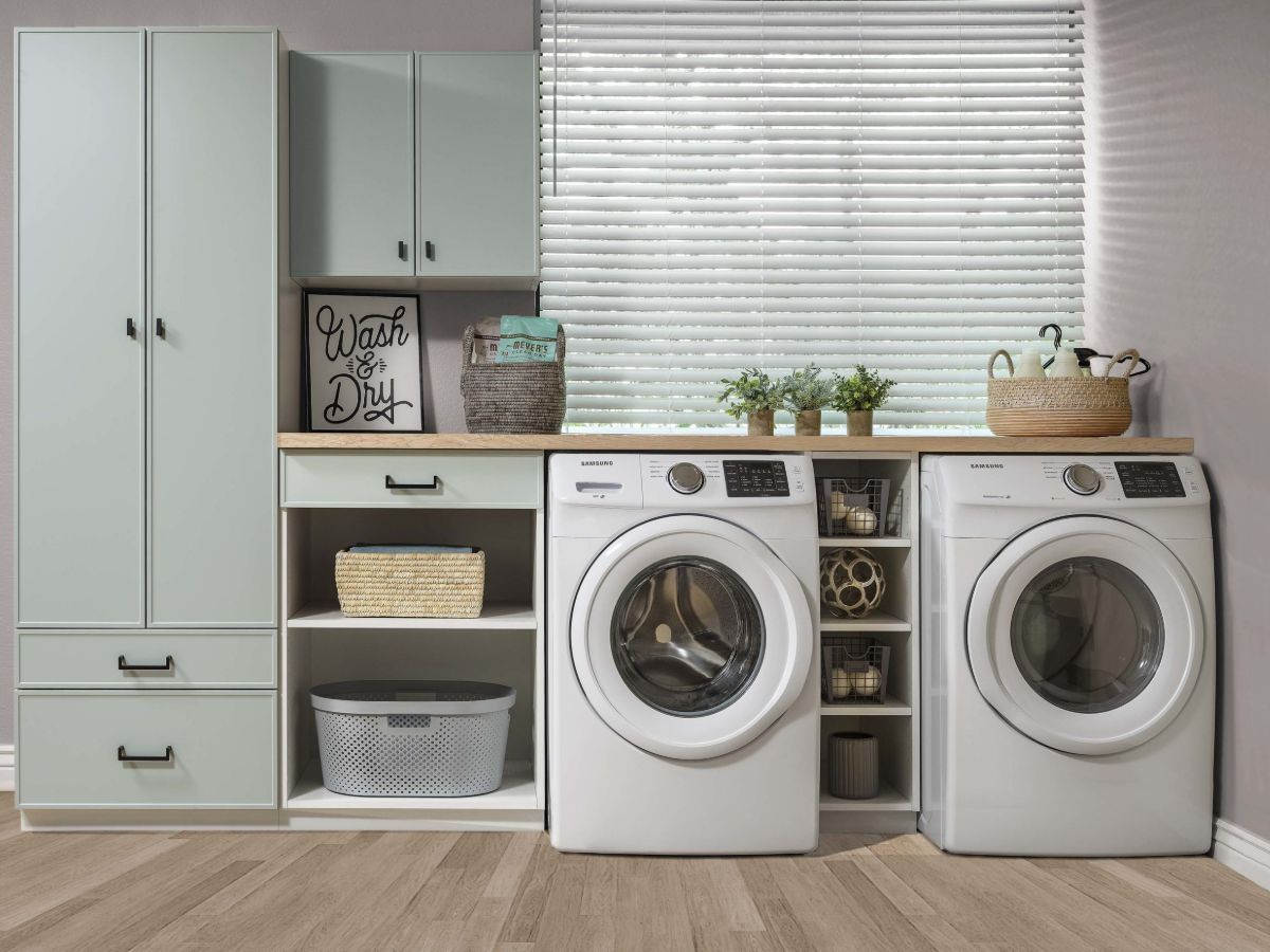 Laundry room with mint-green cabinets, washing machine, dryer, and decorative items.