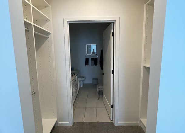 Closet entrance leads to a bathroom. White shelving flanks both sides. The bathroom has a sink and a toilet.