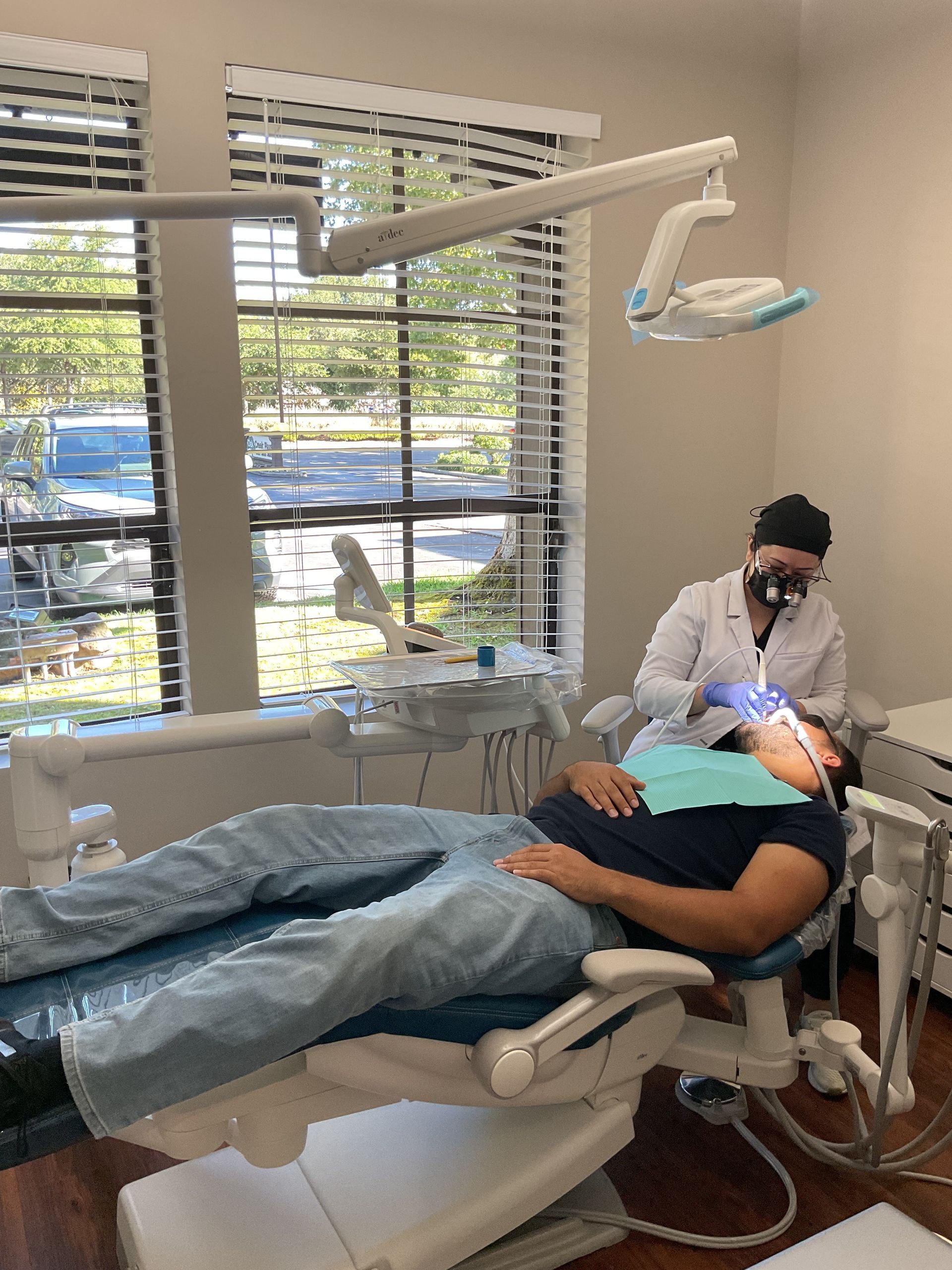 Dentist treating a patient in a dental chair with overhead exam light in a bright office
