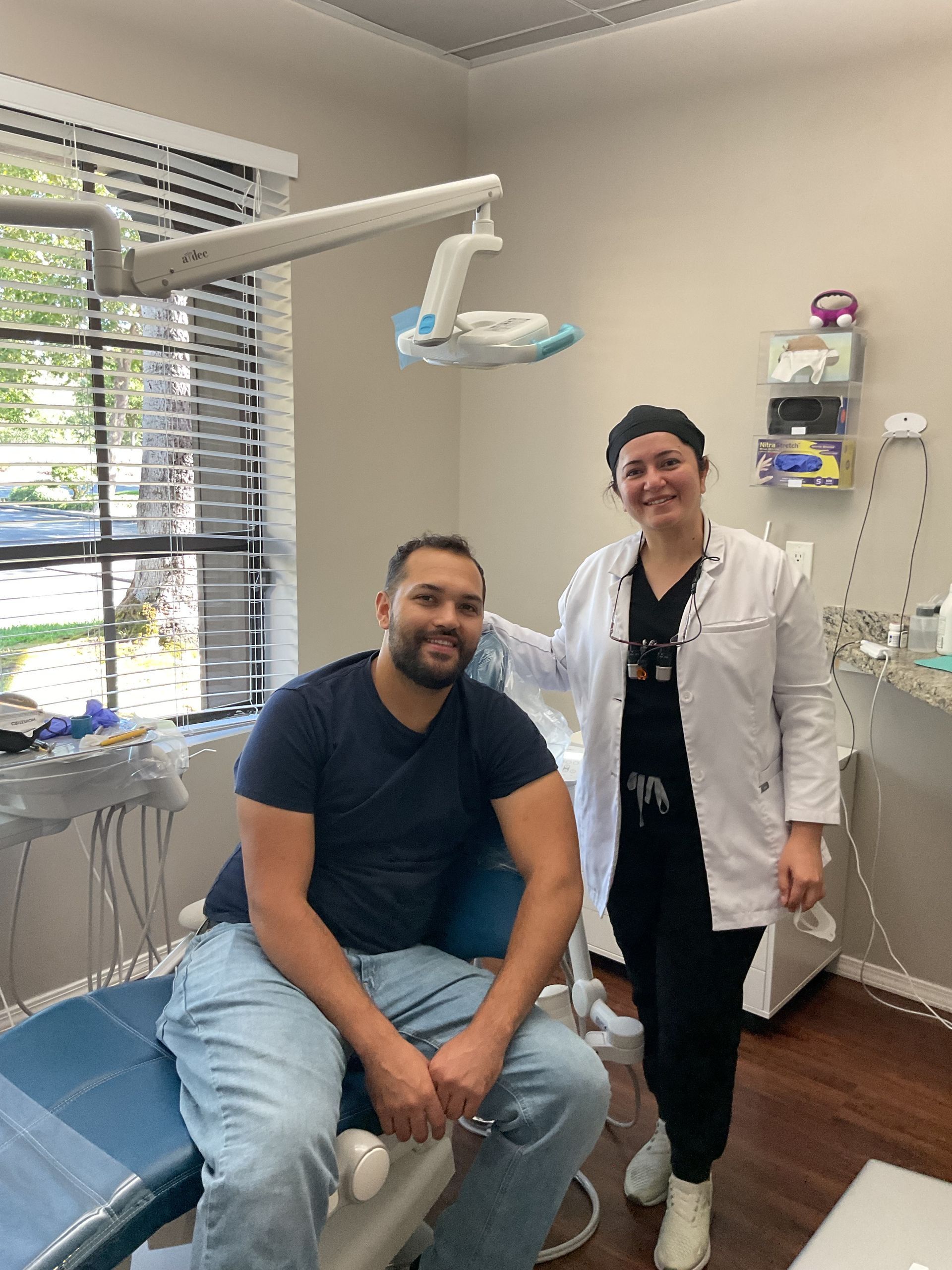 Patient seated in a dental exam room beside a smiling clinician in a white coat