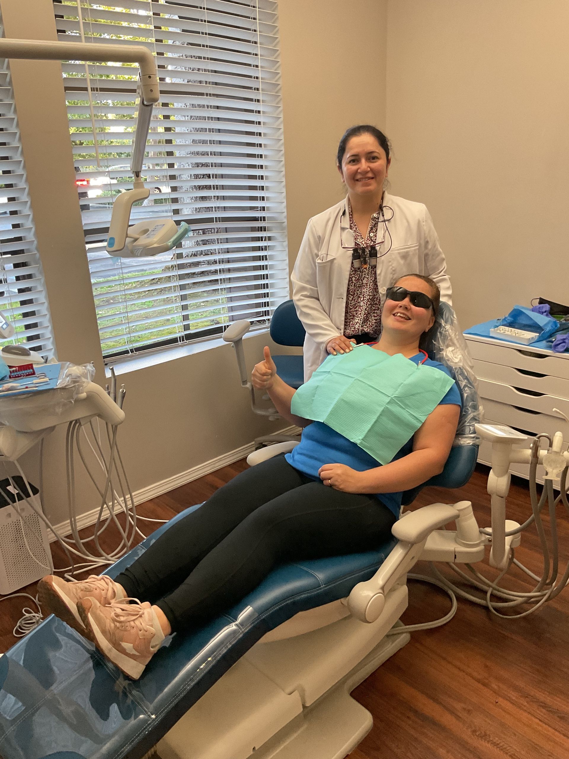 Dental patient reclining in chair while a clinician stands behind her in a bright treatment room.