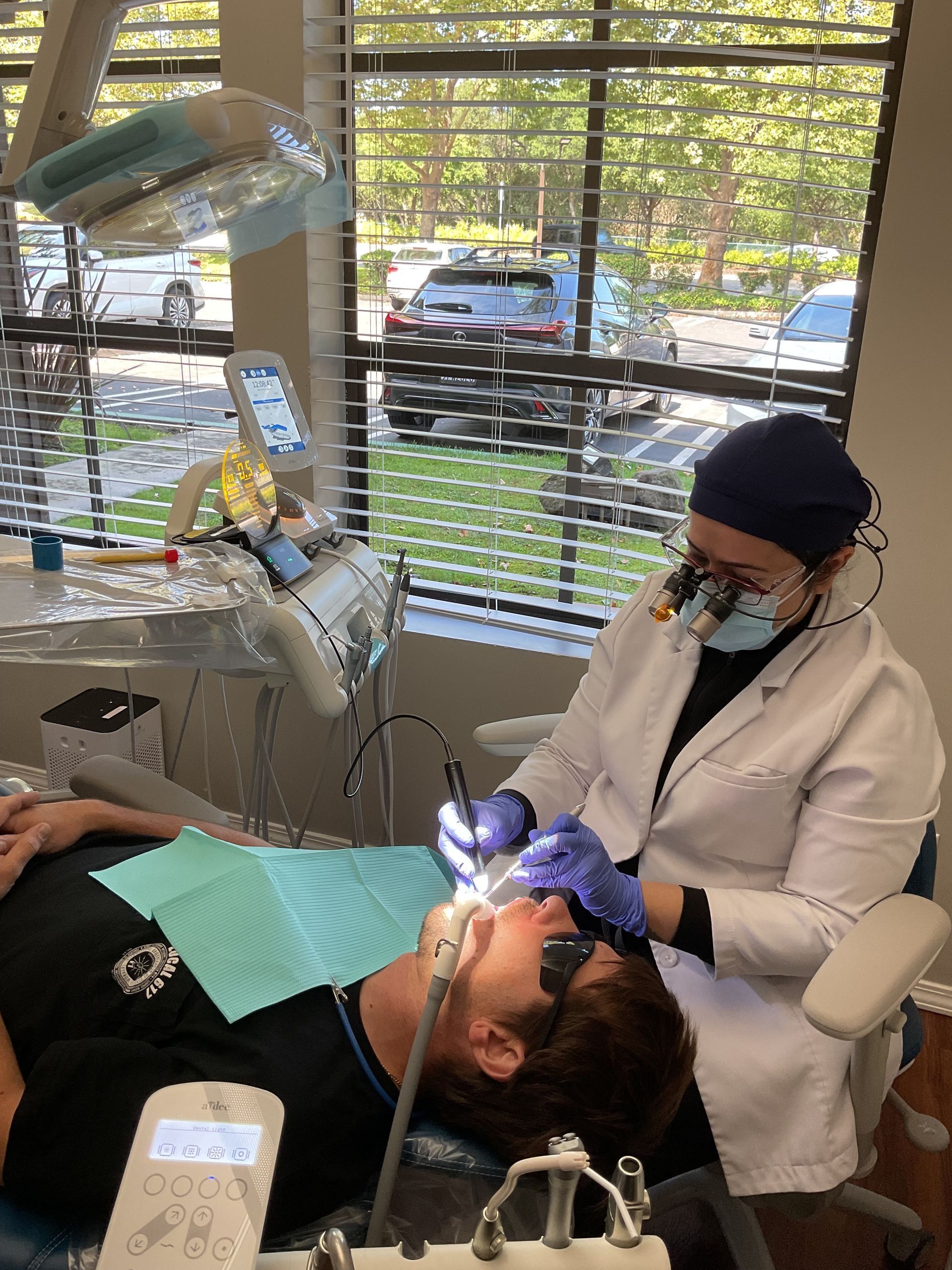 Dental patient receiving treatment while a clinician works beside a window in a bright office