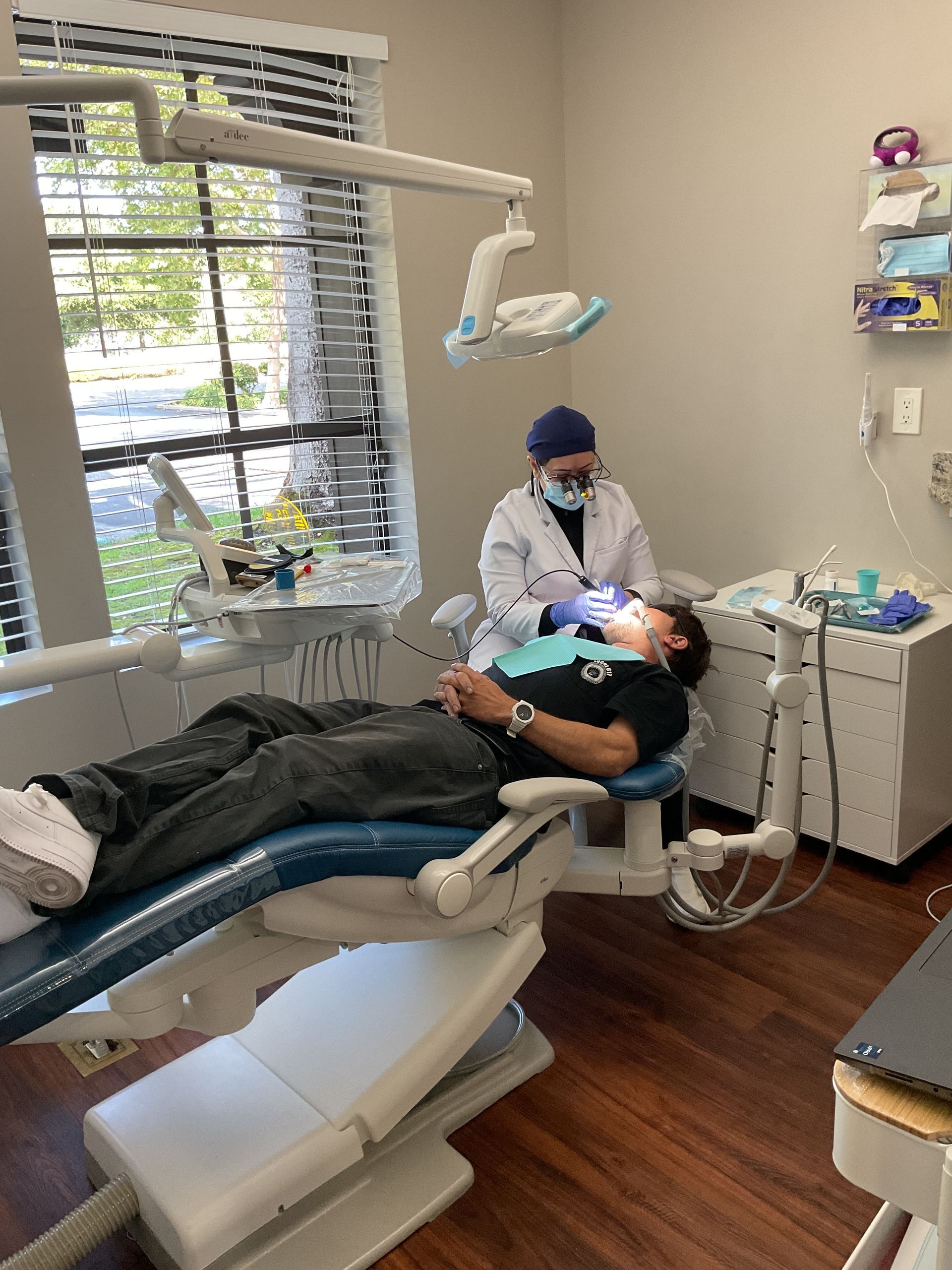 Dentist treating a patient in a modern dental clinic, with reclining chair and overhead light.