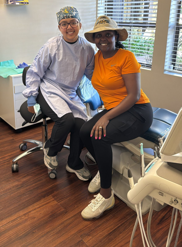 A woman is sitting in a dental chair while a dentist examines her teeth.