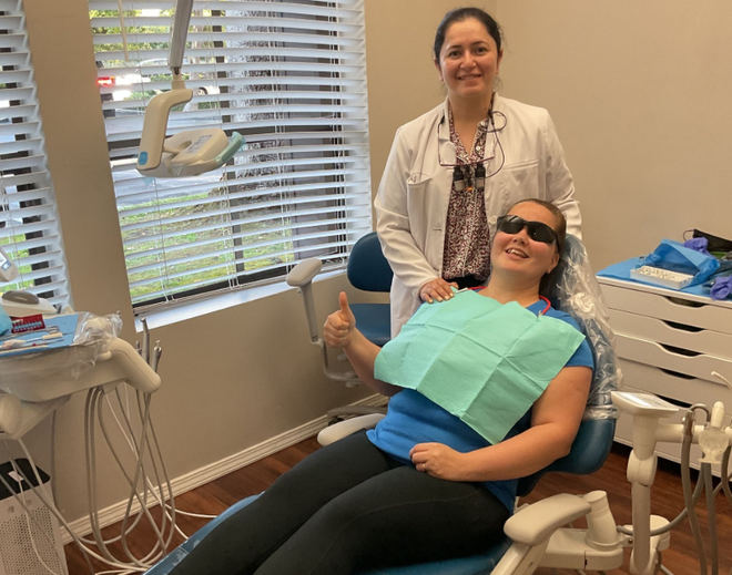 A woman is sitting in a dental chair while a dentist examines her teeth.