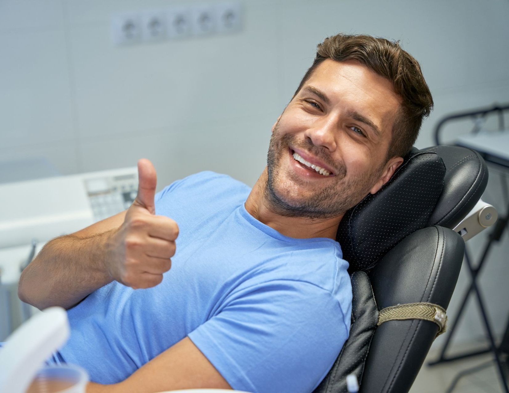 A man is giving a thumbs up while sitting in a dental chair.