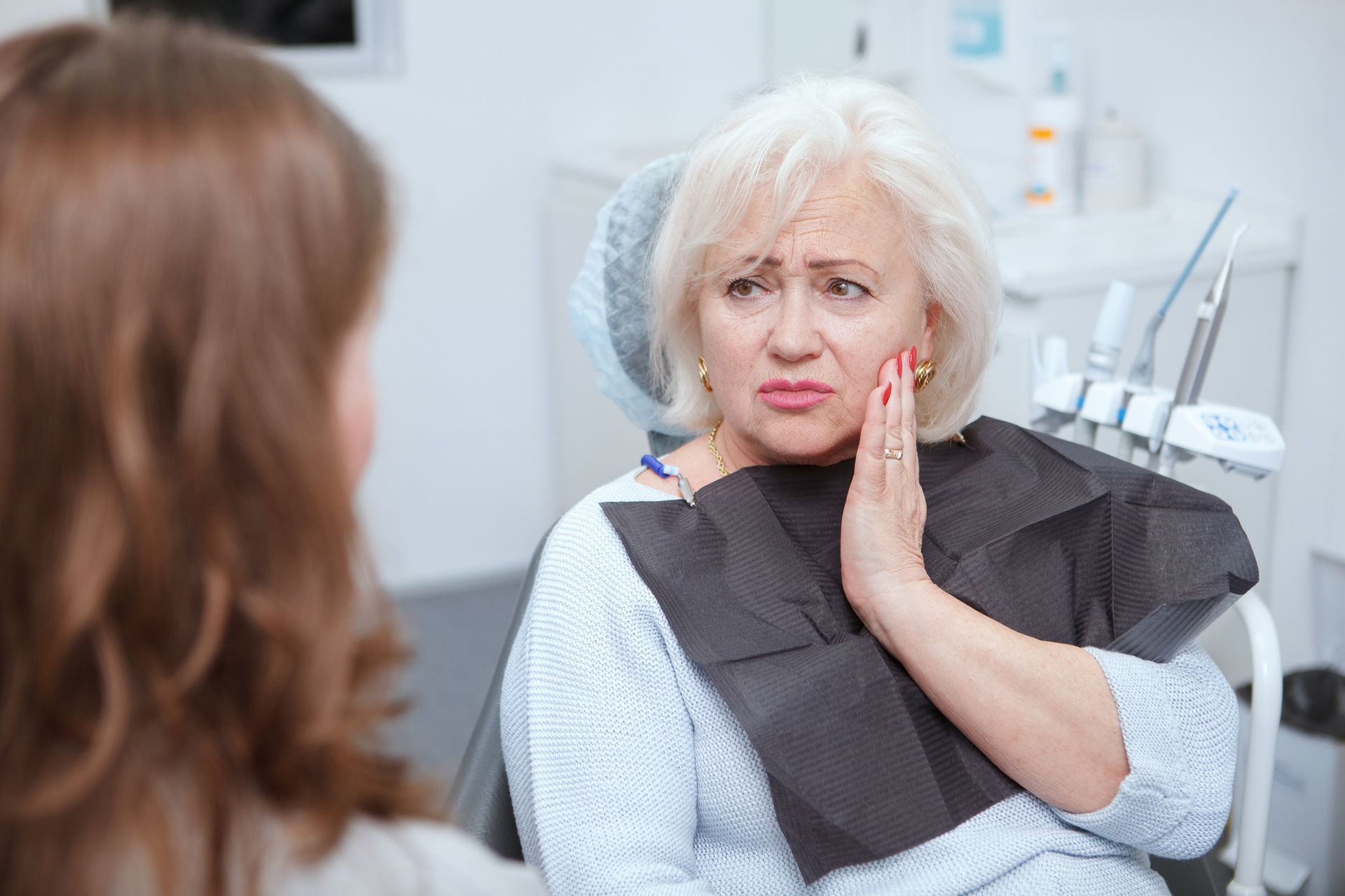 Woman at the dentist's office, holding her jaw in pain. Dentist looks on, concerned.