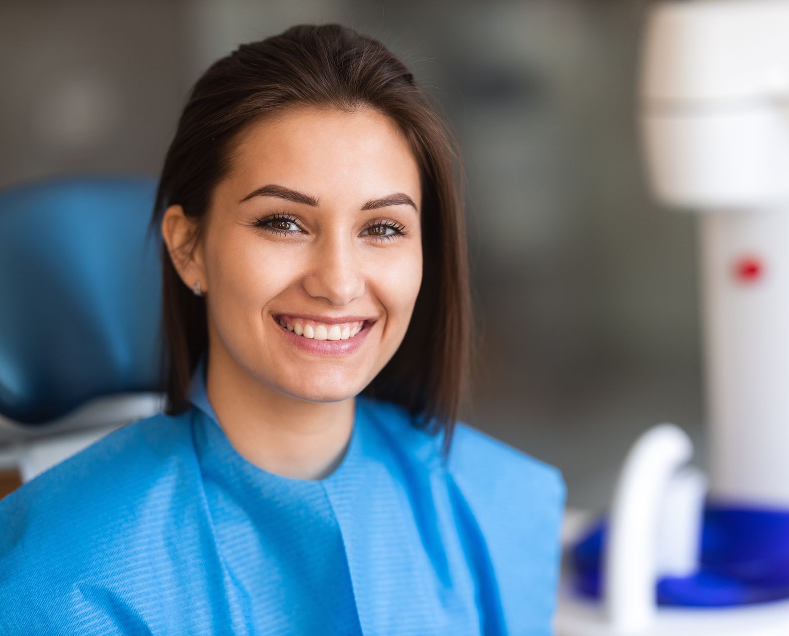 A woman is smiling while sitting in a dental chair.