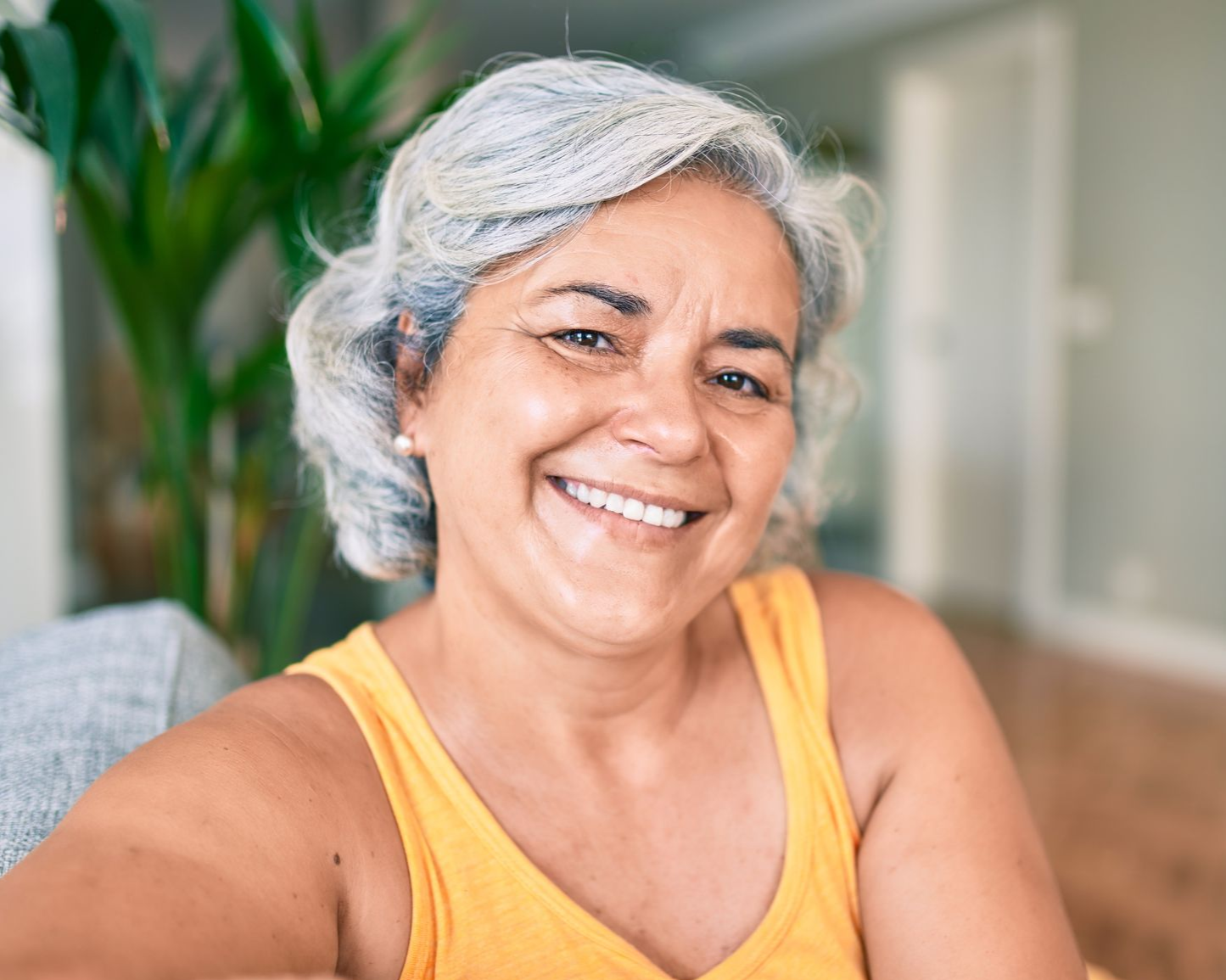 Smiling person with gray hair in a yellow tank top in a bright indoor living room