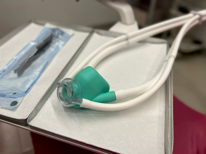 A green nitrous oxide nasal hood with white breathing tubes resting on a tray in a dental office.