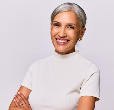 Smiling professional with gray hair in a white shirt, arms crossed against a plain light gray background.