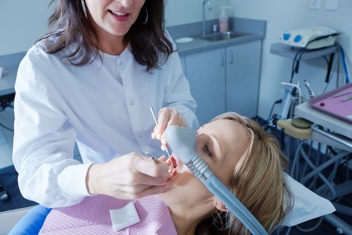 A dental professional examines a patient’s teeth while the patient uses nitrous oxide sedation.