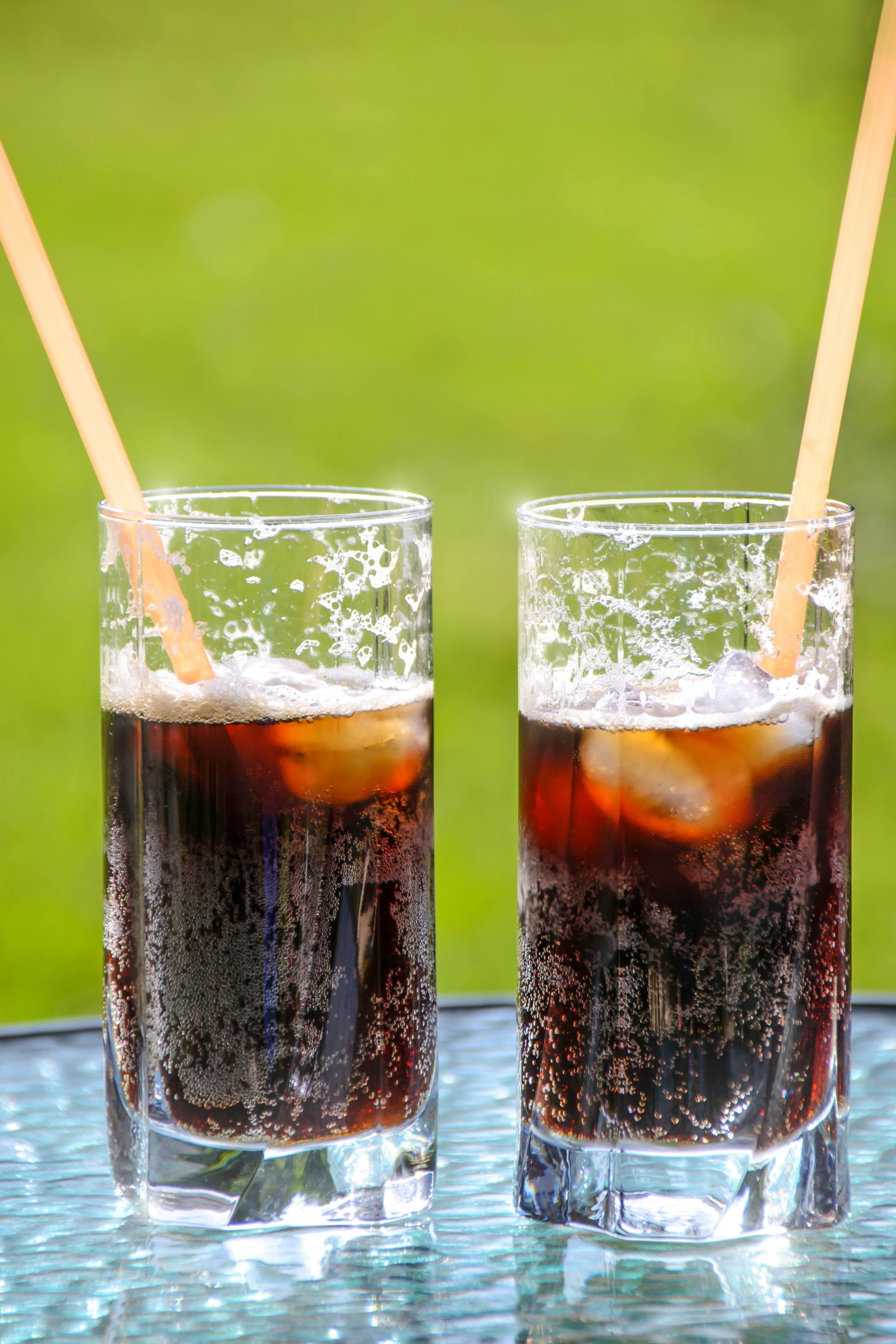 Two glasses of cola with ice cubes and straws on a table.