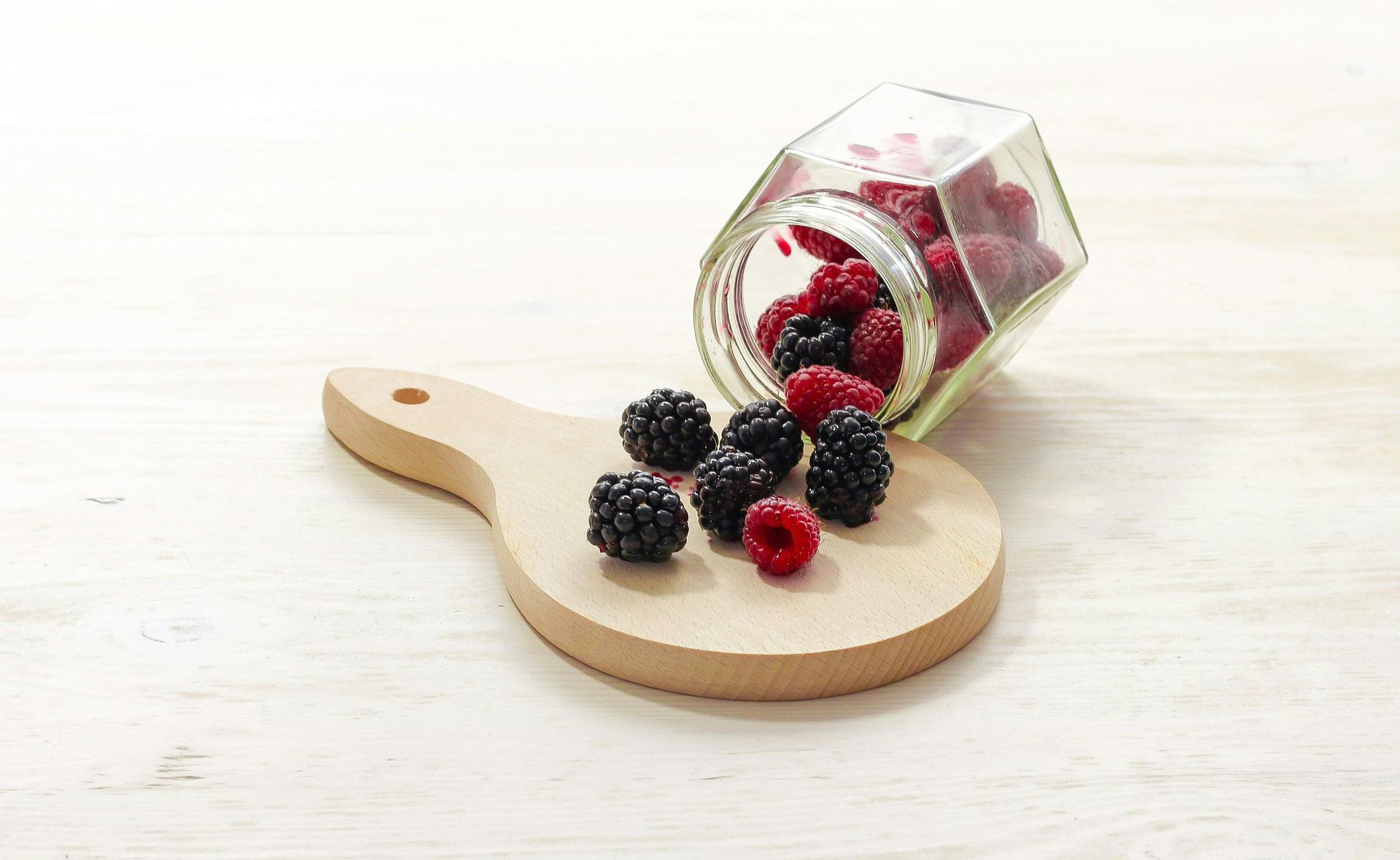 A jar of raspberries and blackberries on a wooden cutting board.