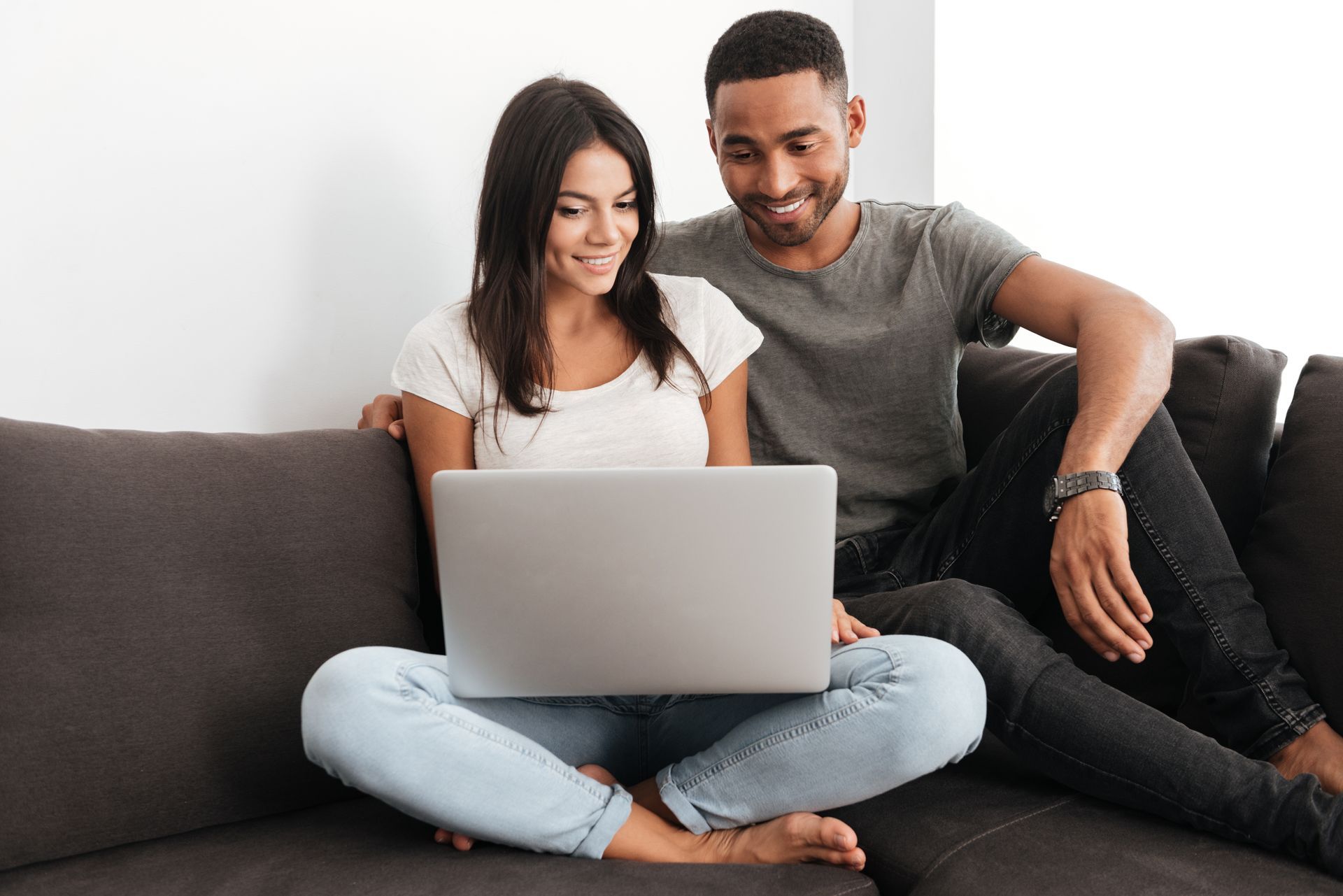 Two people smiling on a couch using a laptop together