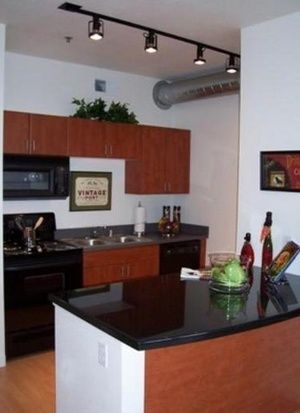 Modern kitchen with black countertops, wood cabinets, track lighting, and a small island.