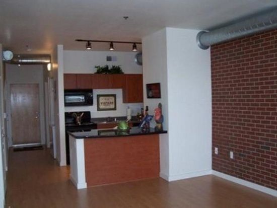 Modern apartment interior with a kitchen island, brick accent wall, and wood flooring