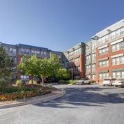 Apartment complex courtyard with brick buildings, trees, and a paved driveway under a clear blue sky