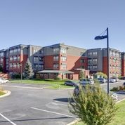 Modern apartment complex with red-brick and gray facades beside a parking lot and streetlamp.