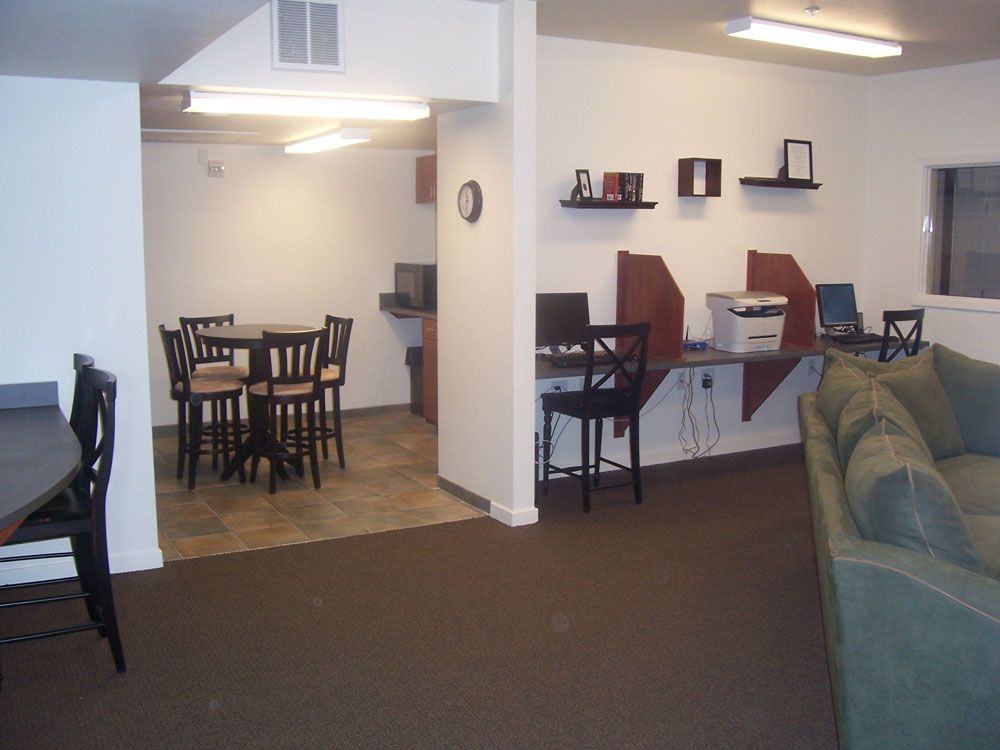 Living room with dining area, desks, chairs, and a green sofa in a modest apartment interior
