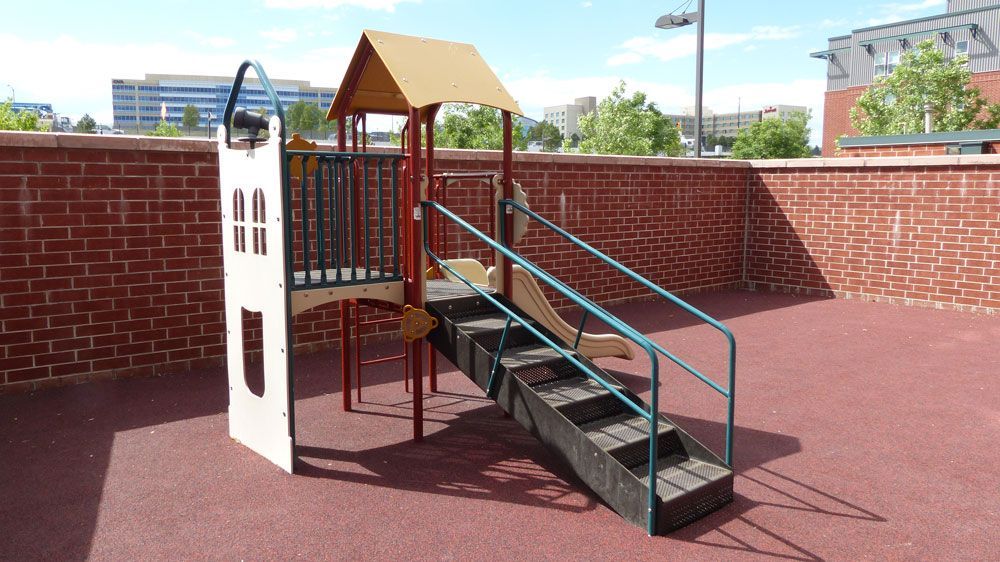 Accessible rooftop playground with stairs, slide, and climbing structure against brick walls