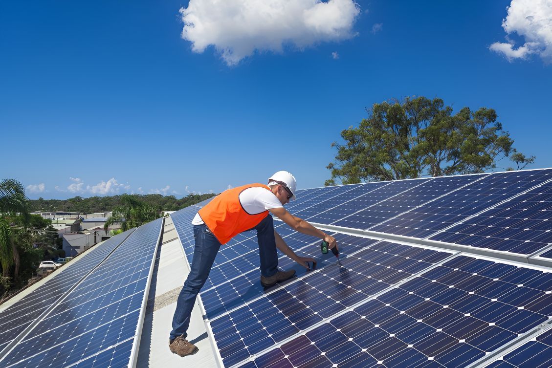 A Man Is Installing Solar Panels On The Roof Of A Building — Entire Power Solutions In Mayfield, NSW