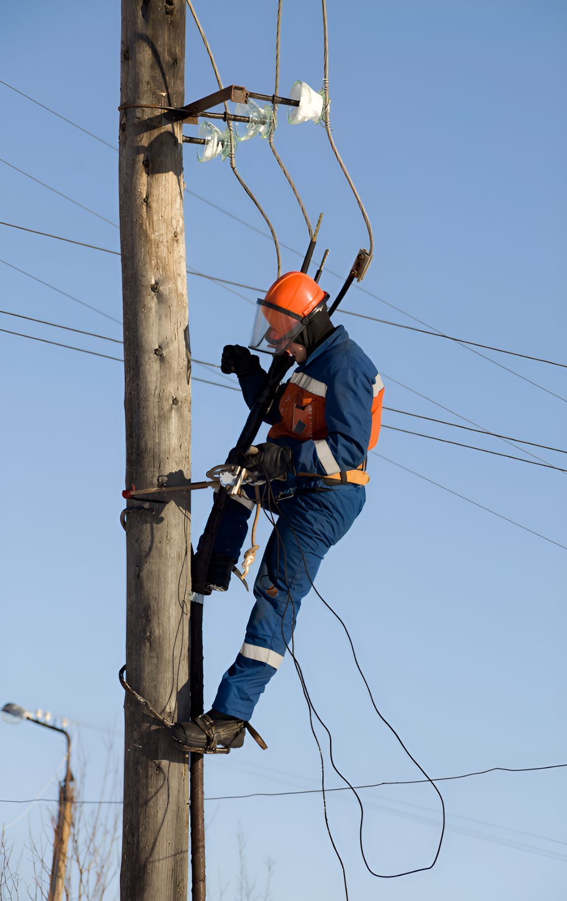 A Man Is Climbing Up A Power Pole With A Chainsaw — Entire Power Solutions In Warners Bay, NSW