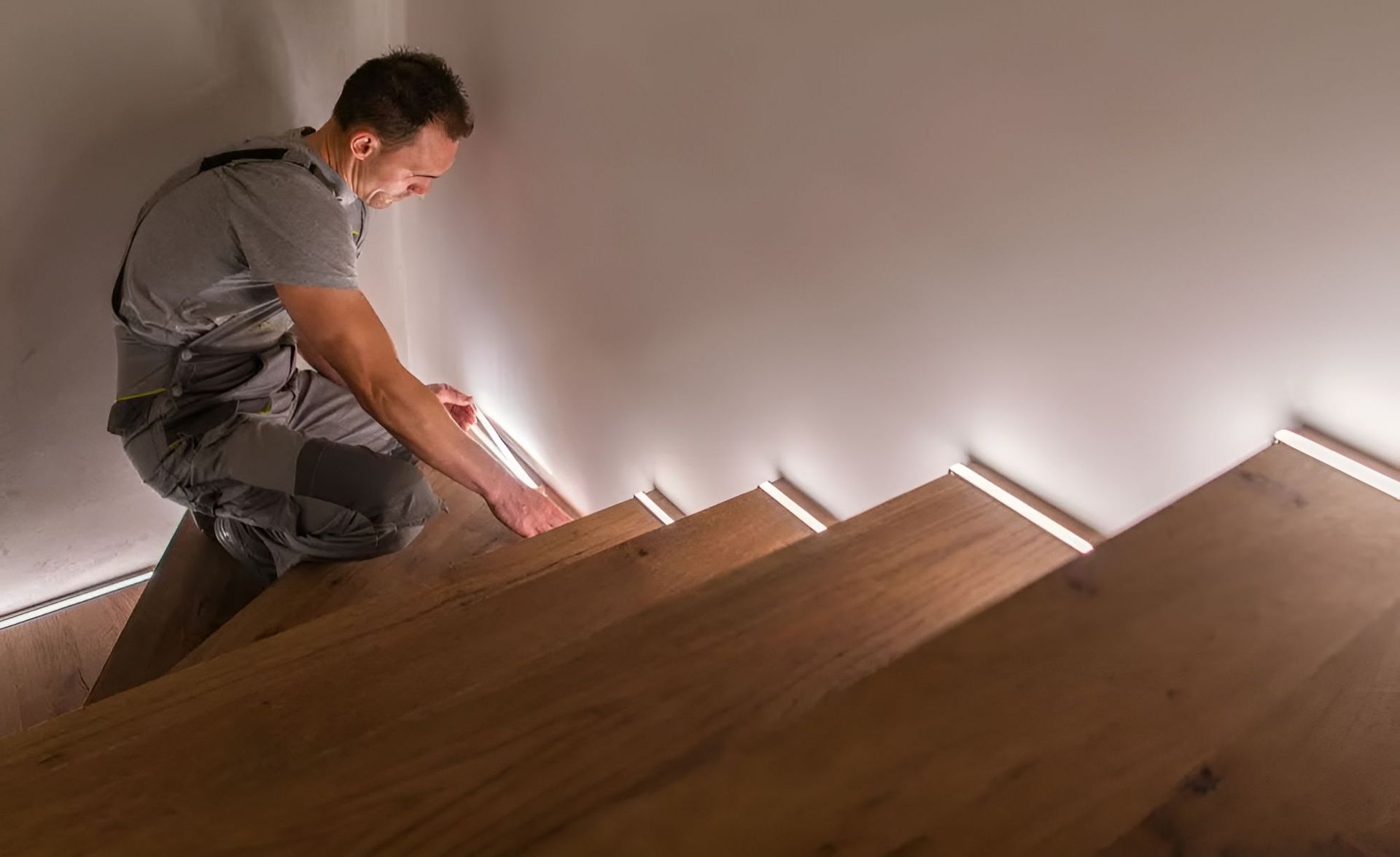 A Man Is Kneeling Down On A Wooden Staircase — Entire Power Solutions In Aberglasslyn, NSW