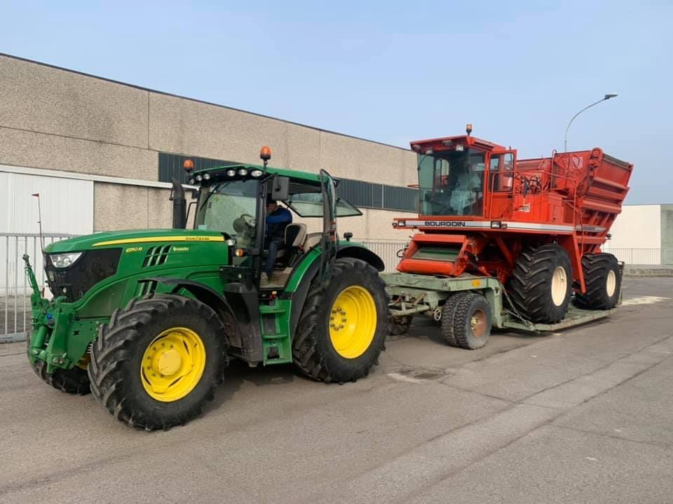 Un trattore verde John Deere traina un trattore rosso su un rimorchio.