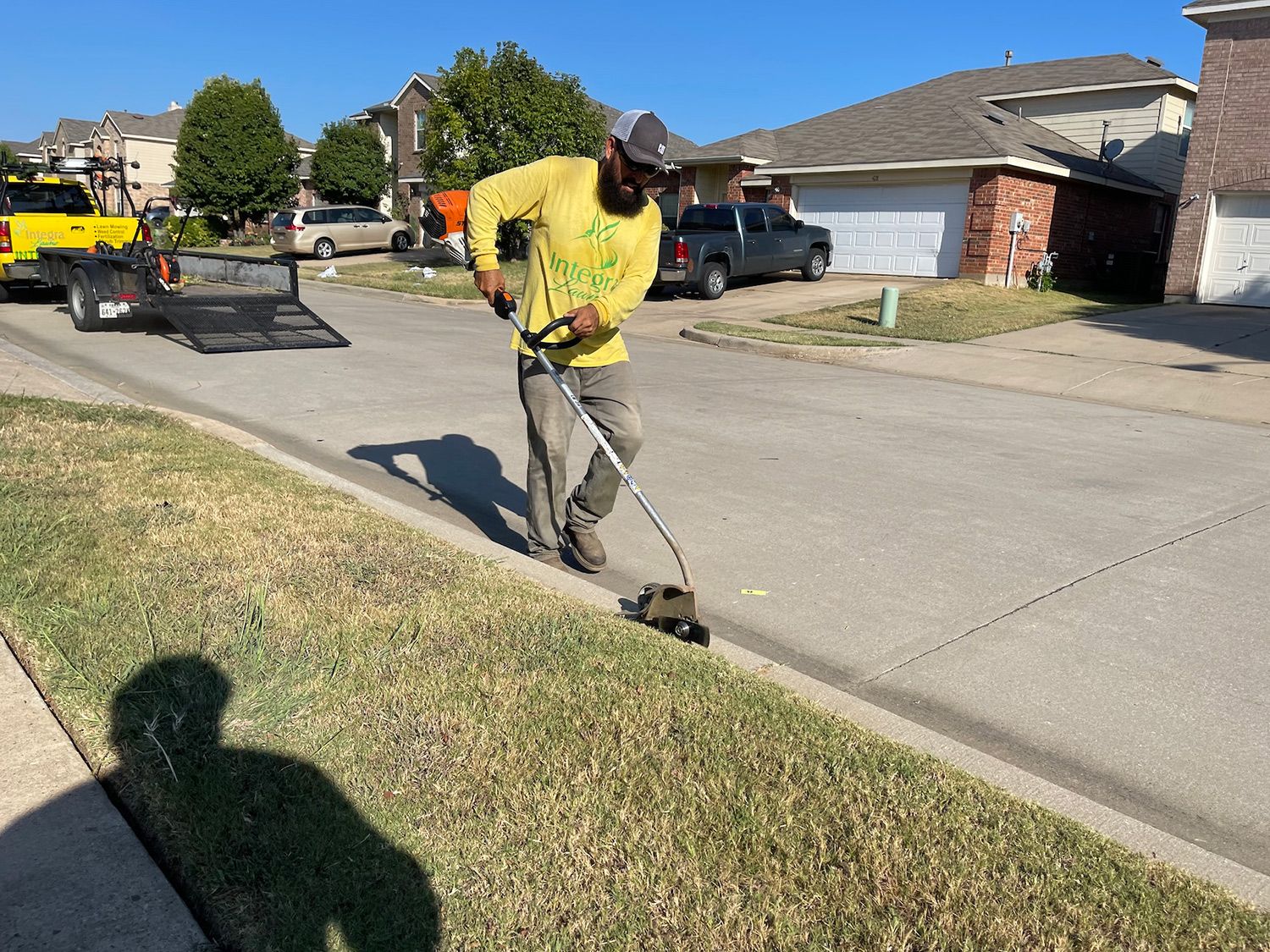 Man in yellow shirt edges grass along a street curb.