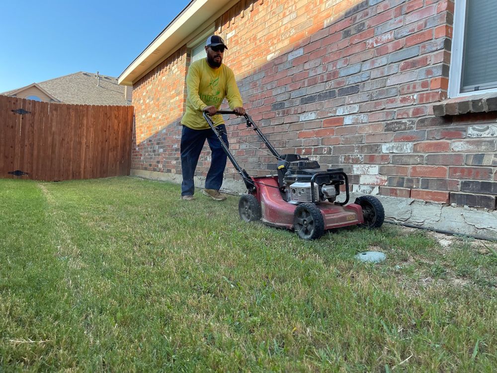 Man mowing a green lawn next to a brick building, sunny outdoors.