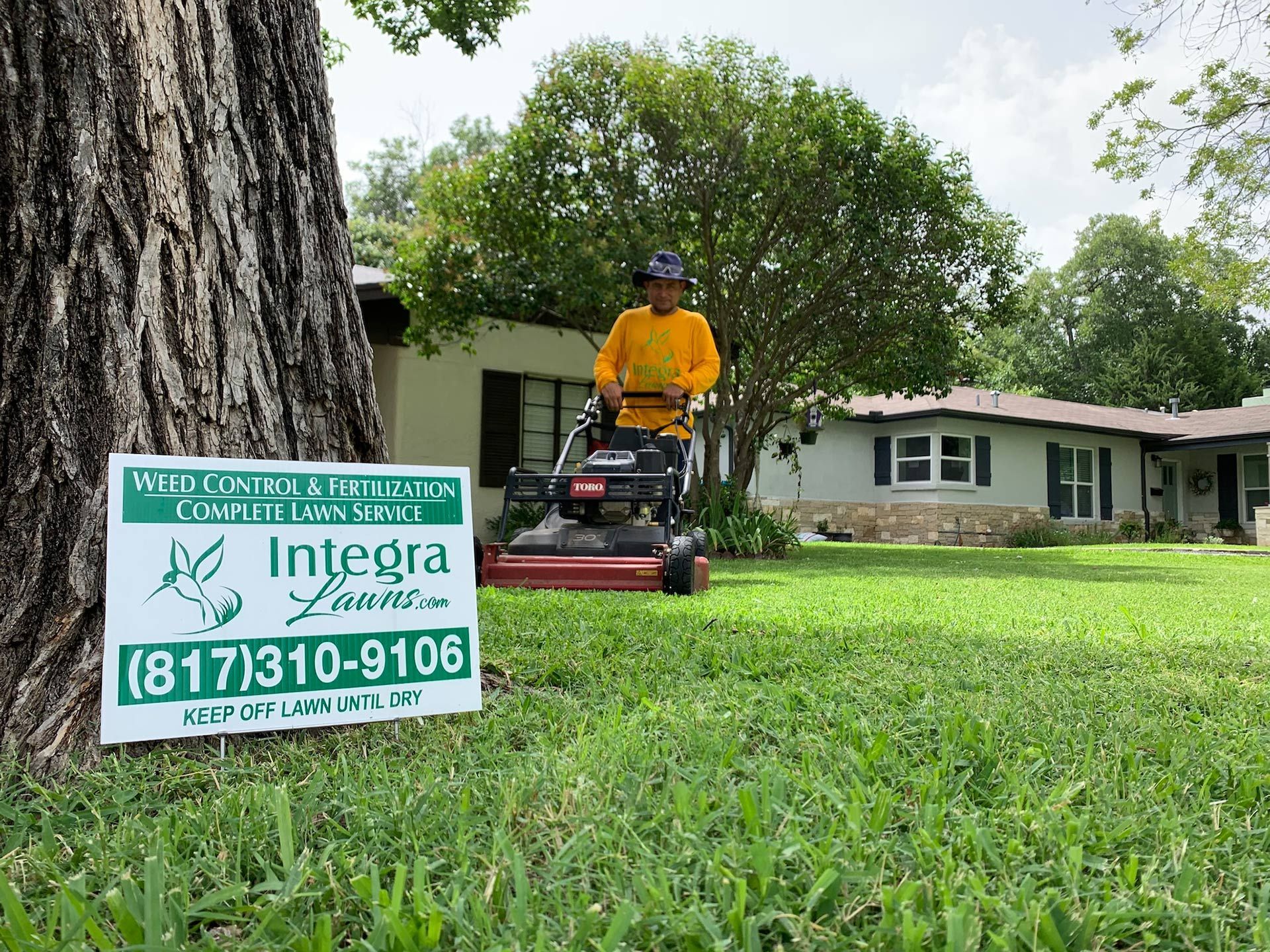 Man mowing a lawn with a Toro mower, with a sign for Integra Lawns in front of a house.