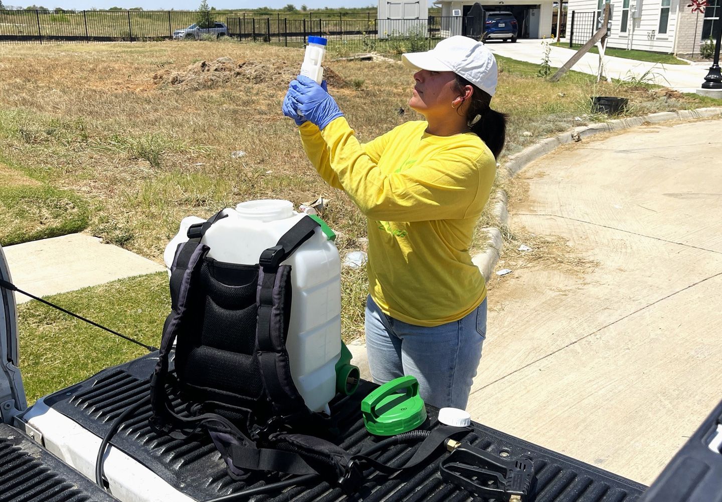 Woman with gloves preparing to spray herbicide from a backpack sprayer in a residential area.