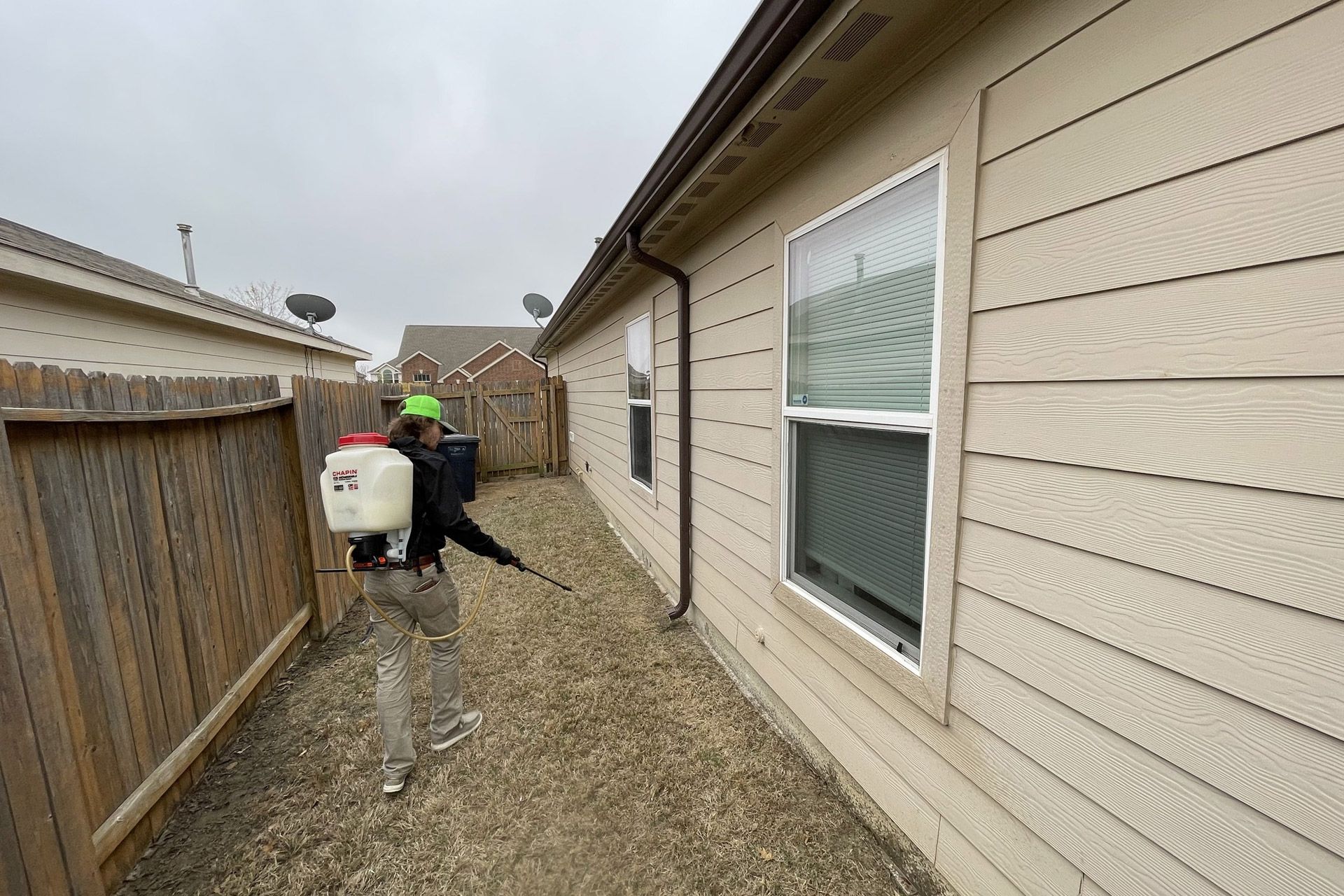 Person spraying insecticide near house and fence.
