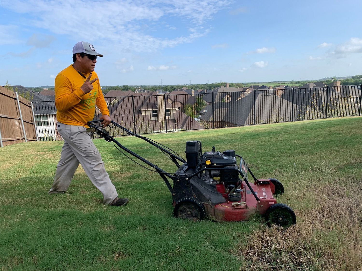 A person aerates grass with a lawn aerator on a sloped yard under a cloudy sky.