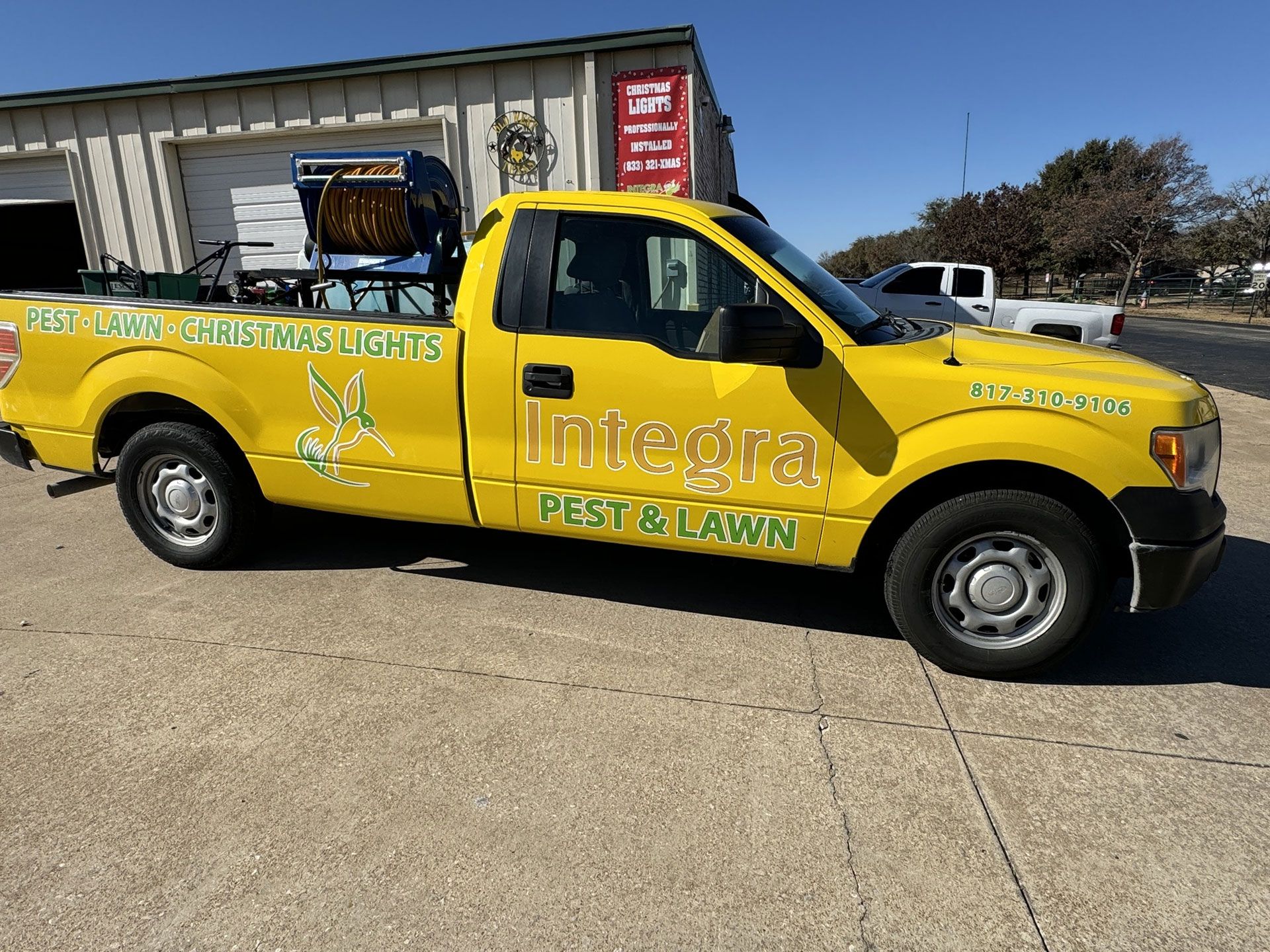 Yellow Integra Pest & Lawn truck with Christmas lights on the back, parked outdoors.