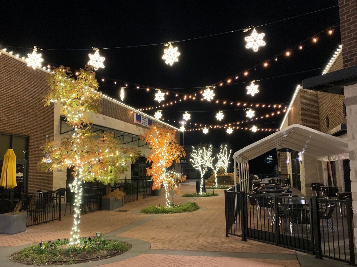 Night view of a brick plaza with trees wrapped in lights and snowflake lights strung overhead.