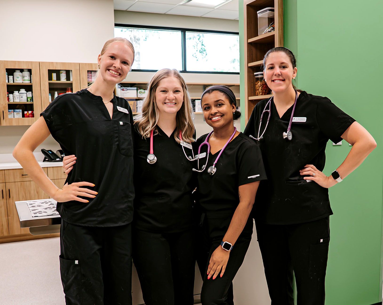 Four medical staff in black scrubs standing together and smiling in a clinic reception area