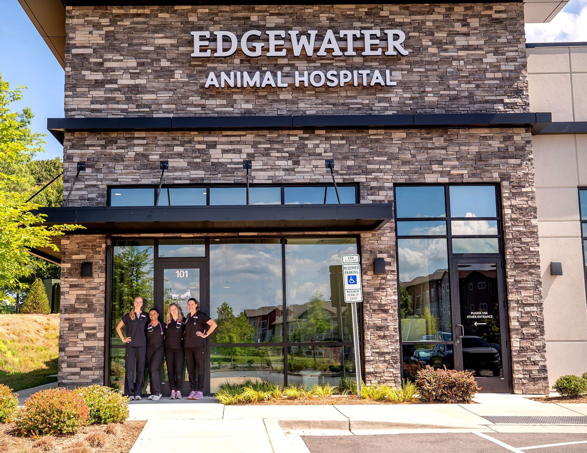 Front entrance of Edgewater Animal Hospital with stone facade and three staff members standing by the glass doors