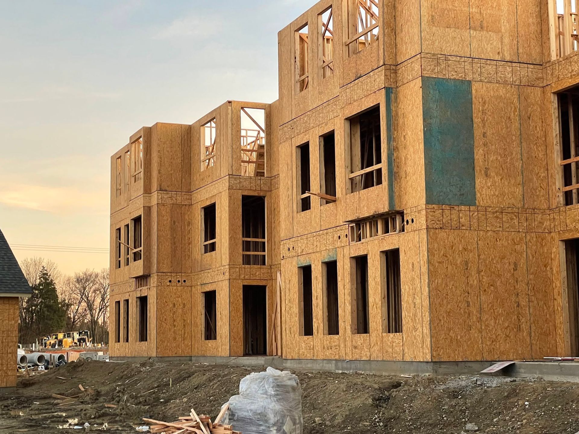 Wood-framed apartment buildings under construction at dusk, with unfinished plywood exteriors and open windows